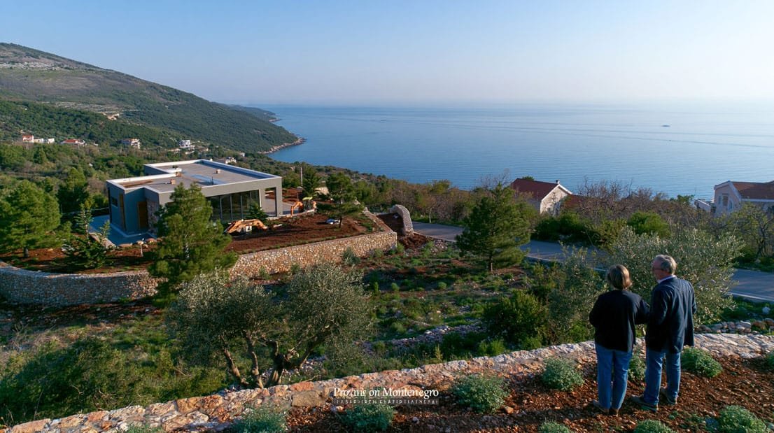 Vorsorgeimmobilie Montenegro - Zwei Personen stehen auf einer Terrasse und betrachten ein modernes Haus nahe der Küste.
