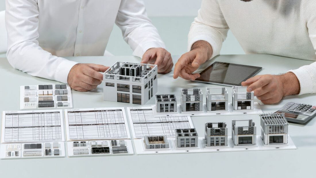 Immobilienkauf - Zwei Personen besprechen Baupläne, Architekturmodelle, ein Tablet und einen Taschenrechner.