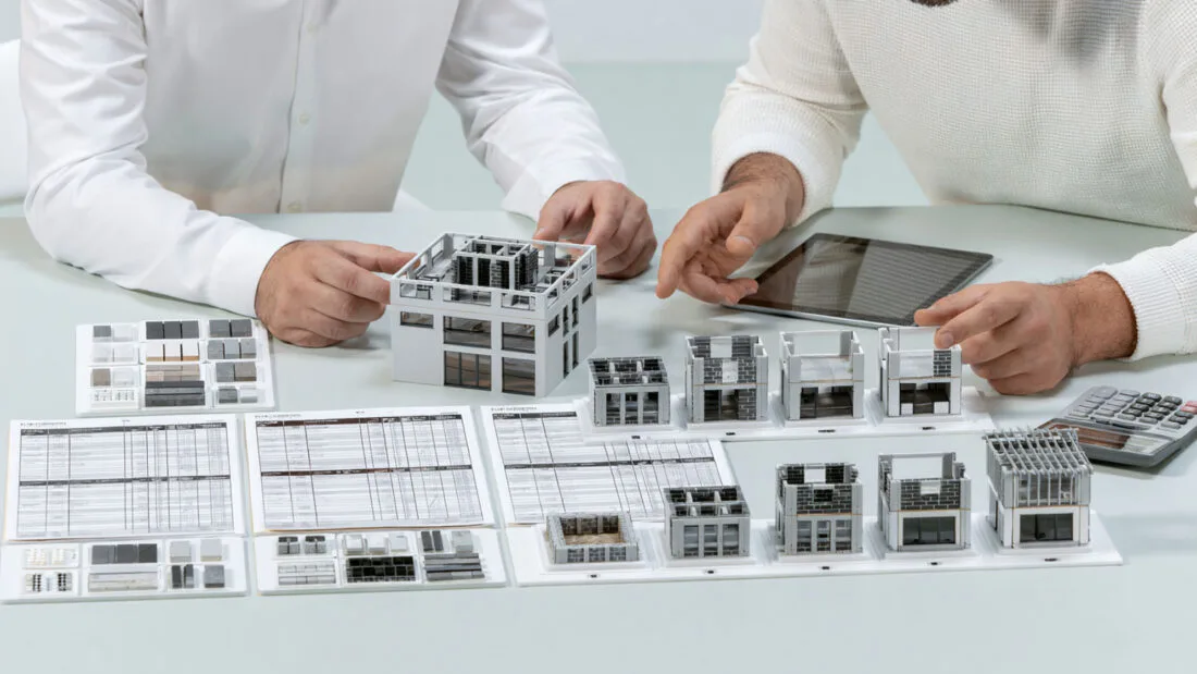 Immobilienkauf - Zwei Personen besprechen Baupläne, Architekturmodelle, ein Tablet und einen Taschenrechner.